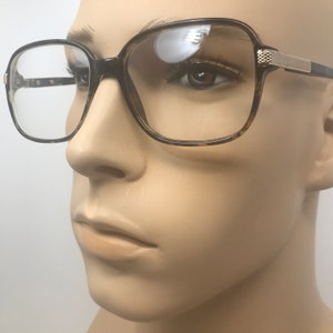 Puede incluir: Gafas de montura cuadrada con un patr&oacute;n de carey en las monturas y varillas. Las gafas tienen lentes transparentes y un acento met&aacute;lico dorado en las varillas. Las monturas est&aacute;n sobre un fondo neutro.
