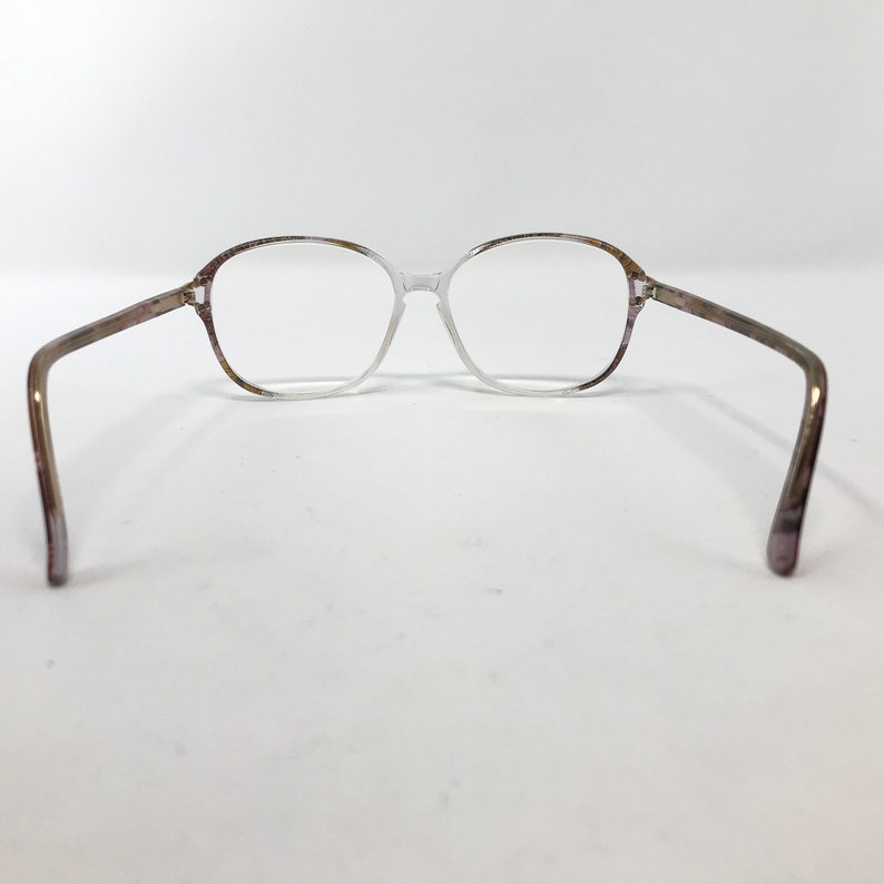 May include: Clear eyeglasses with a light brown and purple speckled pattern on the frame. The glasses have a classic, rectangular shape and are set against a white background.