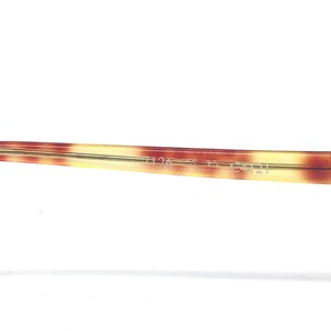 May include: Close-up of a portion of eyeglasses frame with a tortoise shell pattern. The frame is a mix of brown, yellow, and cream colors. The text "7126 56 2 C4121" is printed on the frame.