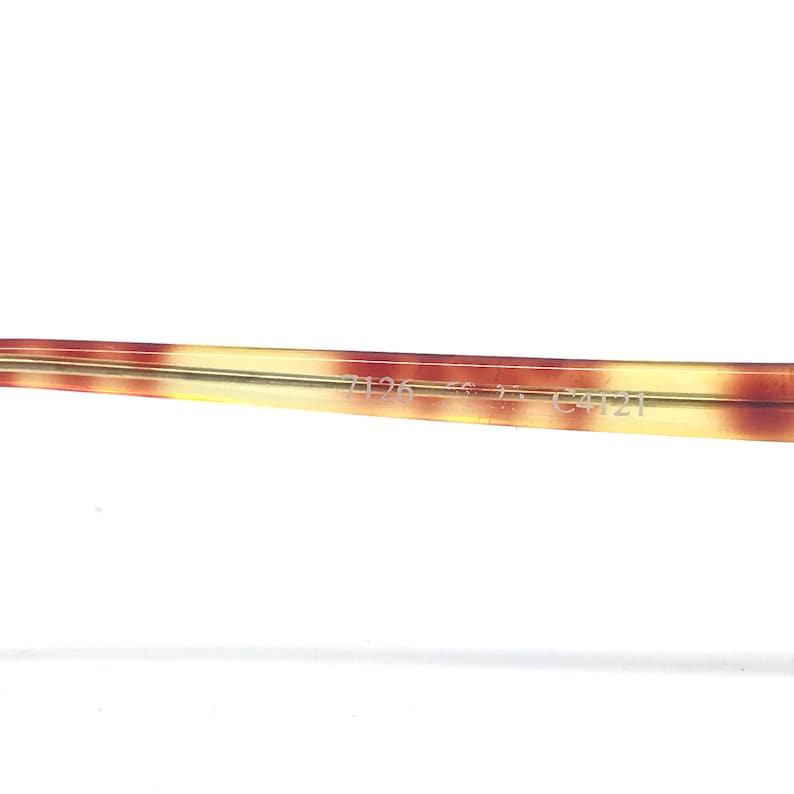 May include: Close-up of a portion of eyeglasses frame with a tortoise shell pattern. The frame is a mix of brown, yellow, and cream colors. The text "7126 56 2 C4121" is printed on the frame.