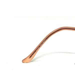 May include: Close-up of a portion of eyeglasses. The frame is a light brown color. The text "513 Fuza 140/4585" is printed on the temple arm. The glasses are set against a white background.