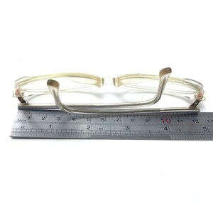 Puede incluir: Gafas con montura de pl&aacute;stico transparente, puente y patillas de metal plateado. Las gafas se miden con una regla, mostrando un ancho de 10 cm.