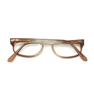 May include: Brown and clear plastic eyeglasses with a rounded frame. The glasses are on a white background.