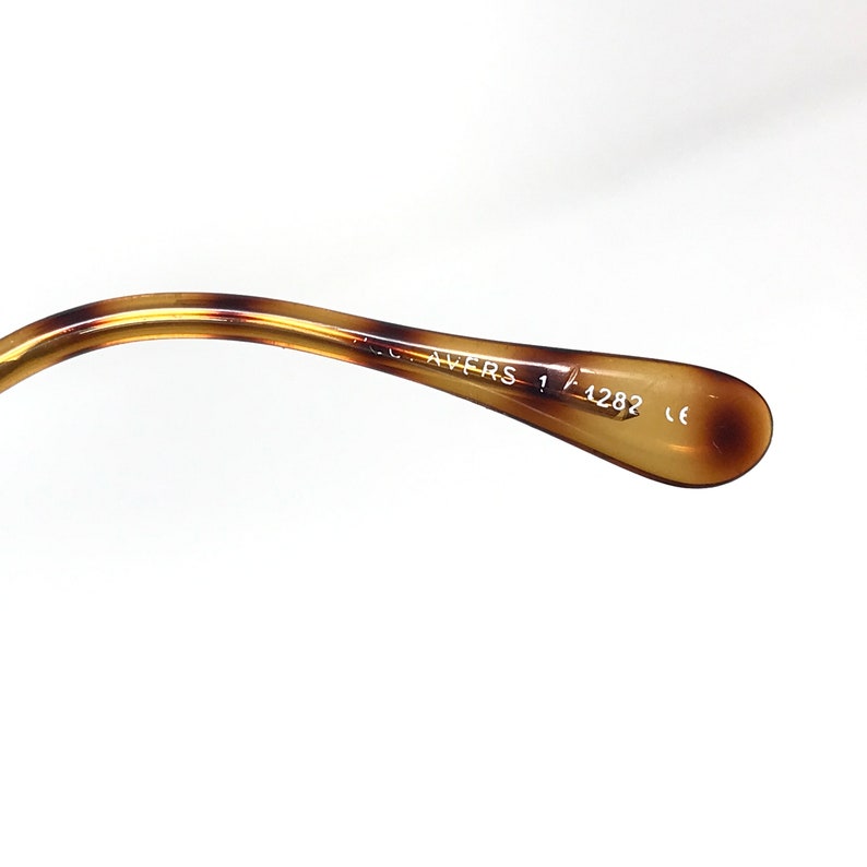 K&ouml;nnte beinhalten: Nahaufnahme der braunen Schildpatt-B&uuml;gelspitze einer Brille. Auf der B&uuml;gelspitze ist der Text "C. Avers 1 1282 CE" aufgedruckt.