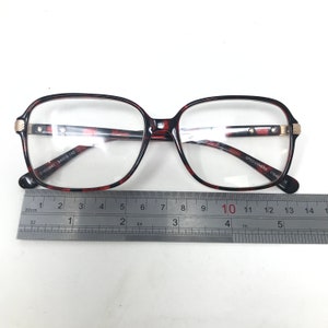 May include: Eyeglasses with a tortoiseshell pattern frame. The glasses have a rectangular shape and clear lenses. The frame has gold-colored accents on the temples. A ruler is placed below the glasses for measurement. The text "SPECSAVERS" is visible.
