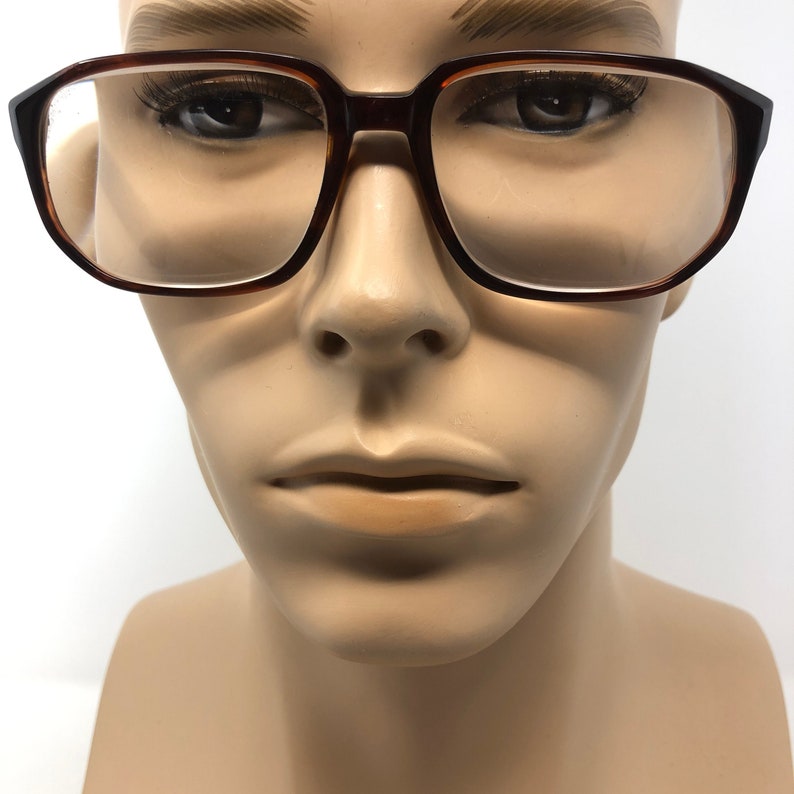 May include: Brown and black eyeglasses with a rectangular frame. The glasses are displayed on a mannequin head. The frames have a tortoiseshell pattern. The lenses are clear.