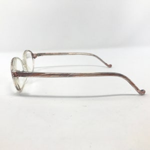 May include: Clear-framed spectacles with round lenses and brown and tan patterned temples. The side view shows the thin, curved arms extending from the frames. The glasses are set against a plain white background.