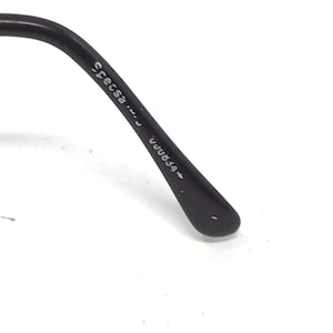 May include: Close-up of the arm of a pair of black eyeglasses. The text "Specsa" and "UUU834" is printed on the arm. The glasses arm is curved and has a rounded tip.