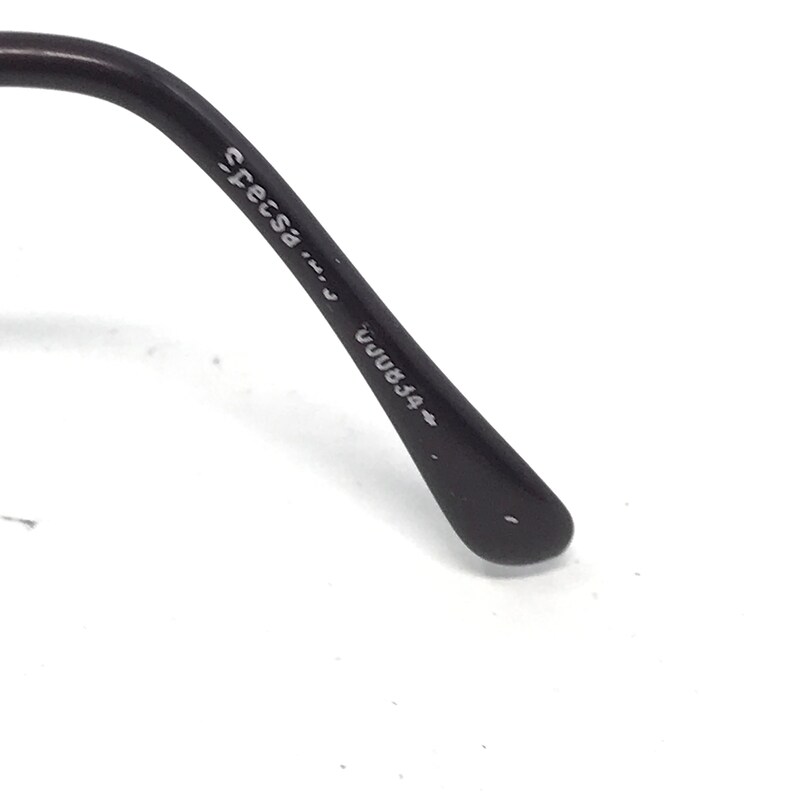 May include: Close-up of the arm of a pair of black eyeglasses. The text "Specsa" and "UUU834" is printed on the arm. The glasses arm is curved and has a rounded tip.