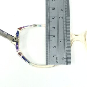 Puede incluir: Gafas transparentes con un patr&oacute;n decorativo en la parte superior de la montura, medidas con una regla. La montura tiene una bisagra plateada y una lente transparente. La regla muestra una medida de aproximadamente 10 cm.