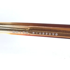 May include: Close-up of the brown and gold frame of a pair of glasses with the text "SMITH 21022098" printed on the inside of the frame.