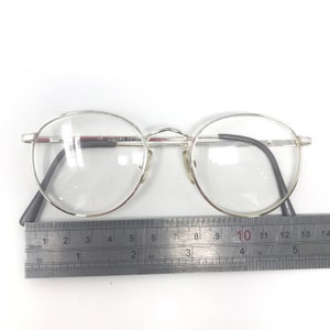 Peut inclure: Lunettes &agrave; monture argent&eacute;e avec verres ronds. Les lunettes ont des branches gris fonc&eacute; et un pont argent&eacute;. Une r&egrave;gle est plac&eacute;e en dessous, mesurant en centim&egrave;tres. Le texte "SPERS FP" est visible sur la monture.