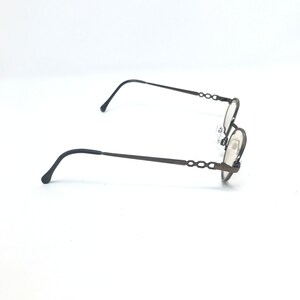 May include: A pair of oval-shaped eyeglasses with a dark brown metal frame. The temples and the frame around the lenses have a decorative chain-link design. The lenses are clear, and the nose pads are visible.