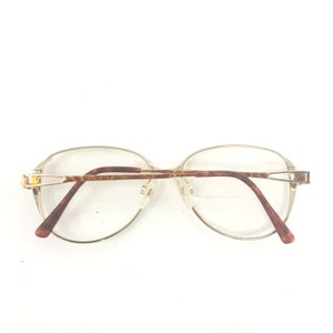 K&ouml;nnte beinhalten: Ovale Brille mit einem goldfarbenen Metallrahmen und braunen Schildpattb&uuml;geln. Die Gl&auml;ser sind klar, und die Nasenpads sind transparent. Die Brille ist f&uuml;r die Sehkorrektur bestimmt und hat einen klassischen, eleganten Stil.