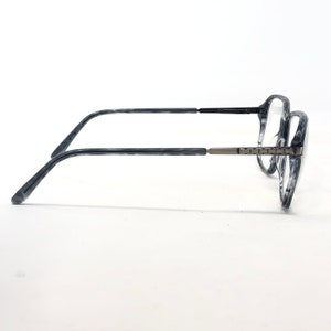 May include: A pair of eyeglasses featuring frames with a marbled grey and black pattern. The thin temples are black, and the hinges are silver-coloured. The clear lenses are set in a modern, stylish design, suitable for everyday wear.