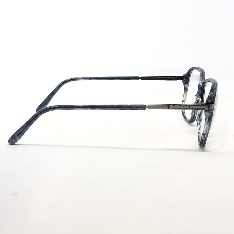 May include: A pair of eyeglasses featuring frames with a marbled grey and black pattern. The thin temples are black, and the hinges are silver-coloured. The clear lenses are set in a modern, stylish design, suitable for everyday wear.