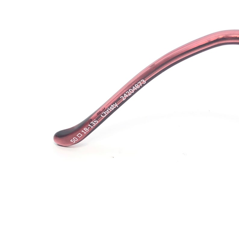 Puede incluir: Primer plano de la patilla de unas gafas. La montura es de color marr&oacute;n rojizo transl&uacute;cido. El texto "50 ▢ 18-135 Christy 24204873" est&aacute; impreso en blanco en la patilla.