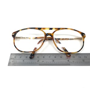K&ouml;nnte beinhalten: Schildpatt-Brille mit goldenen Akzenten und klaren Gl&auml;sern. Die Brille wird mit einem Lineal gemessen.