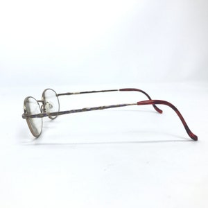 May include: A pair of gold-toned spectacles with a purple and gold patterned frame and red plastic temple tips.