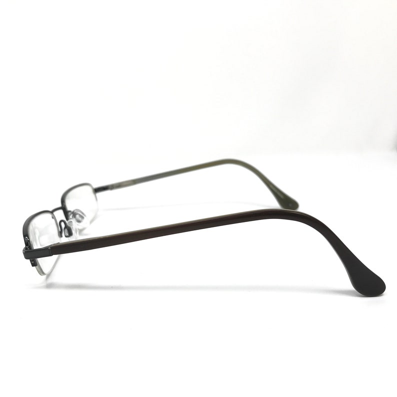 K&ouml;nnte beinhalten: Eine rechteckige Brille mit einem dunkelgrauen Metallrahmen und B&uuml;geln. Die Gl&auml;ser sind klar, und die B&uuml;gel biegen sich sanft zum Ohr hin. Auf wei&szlig;em Hintergrund.