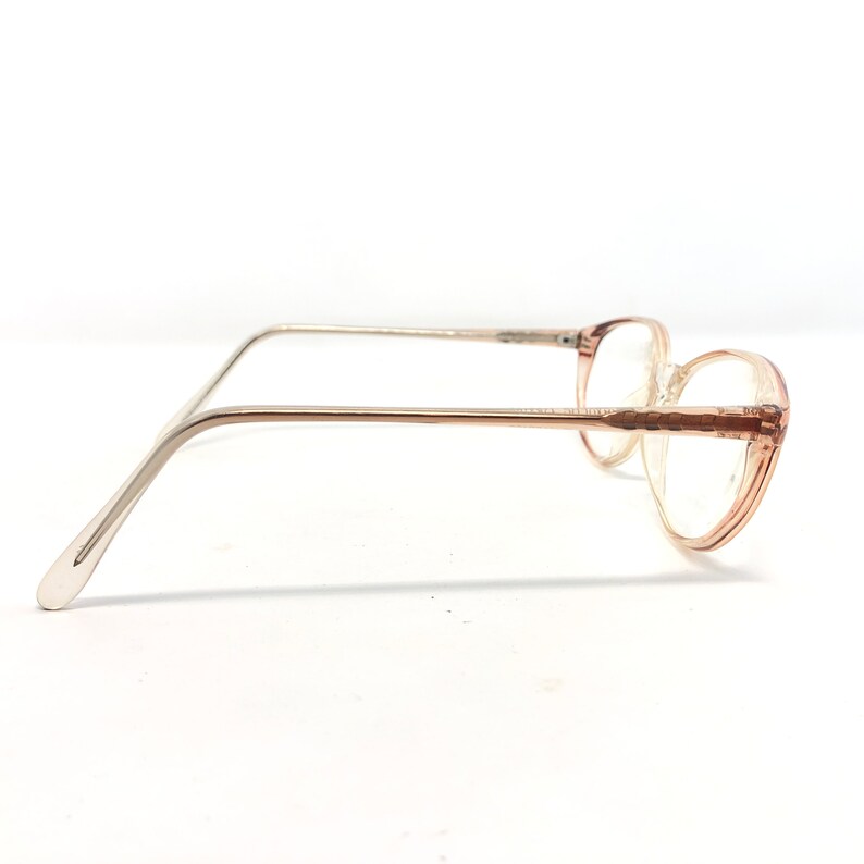 May include: Vintage eyeglasses with a light brown frame and clear lenses. The glasses have a rounded shape and silver-coloured arms. The frame appears to be made of plastic. The glasses are set against a white background.
