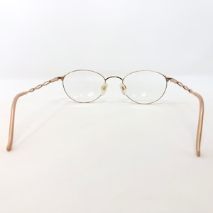 K&ouml;nnte beinhalten: Goldfarbene Brille mit ovalen Gl&auml;sern und einem filigranen, gedrehten Design an den B&uuml;geln. Die Fassungen haben einen dezenten metallischen Glanz, und die Gl&auml;ser sind klar. Das Gesamtdesign ist minimalistisch und elegant.
