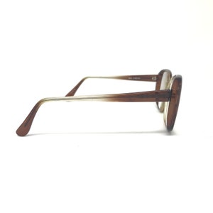 May include: Brown-framed eyeglasses with a square shape. The frames transition from a light to a darker brown. The temples are thin and light-colored, with a curved end for a comfortable fit. The lenses are clear.