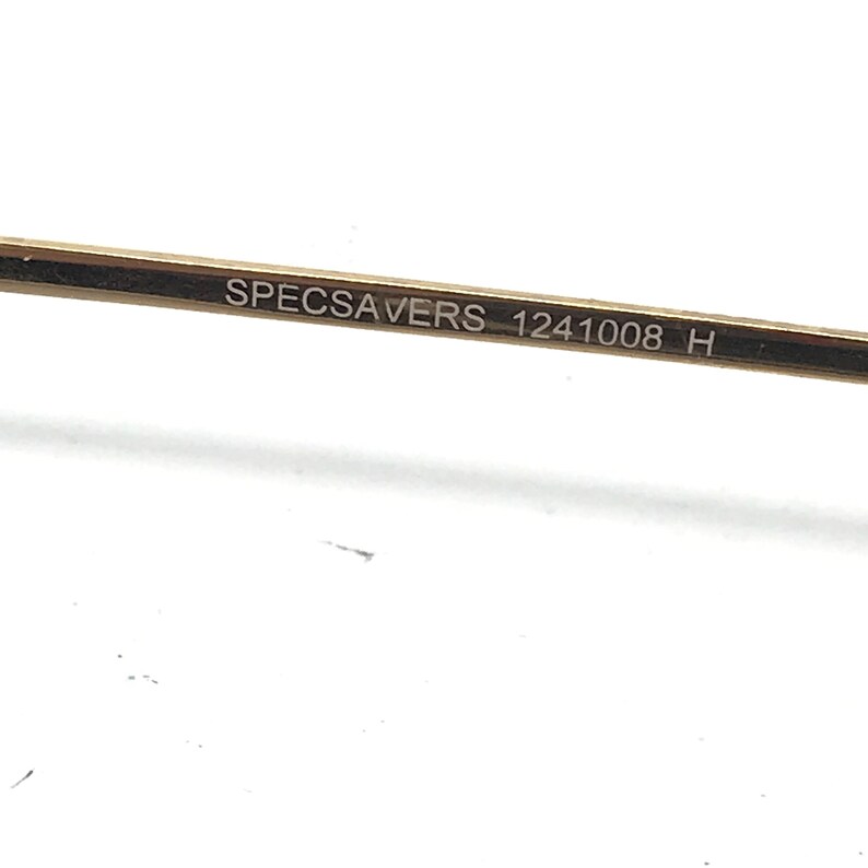 Pu&ograve; includere: Primo piano del braccio di un paio di occhiali dorati con il testo "SPECSAVERS 1241008 H" inciso sul braccio.