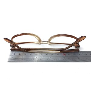 May include: Brown plastic framed glasses with clear lenses. The glasses are measured with a ruler, showing a length of 10 centimeters.
