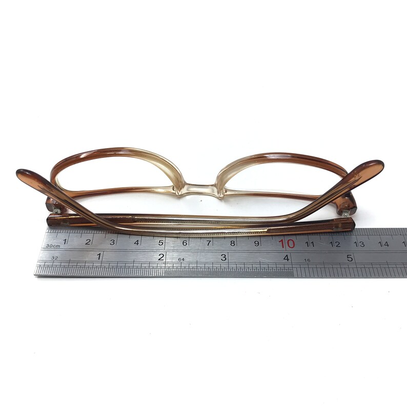 May include: Brown plastic framed glasses with clear lenses. The glasses are measured with a ruler, showing a length of 10 centimeters.