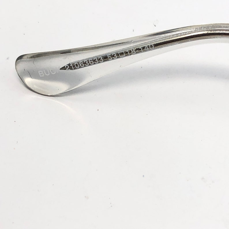 K&ouml;nnte beinhalten: Nahaufnahme des B&uuml;gels einer transparenten Brille. Auf dem B&uuml;gel ist der Text "BUCK" aufgedruckt, zusammen mit den Zahlen "21063633 53[]18-140". Der B&uuml;gel besteht aus einem transparenten Material.