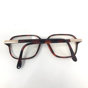 May include: Eyeglasses with a tortoiseshell pattern frame and clear lenses. The rectangular frames have a gold-colored metal accent on the temples. The arms are dark brown and curve down to the ear pieces.