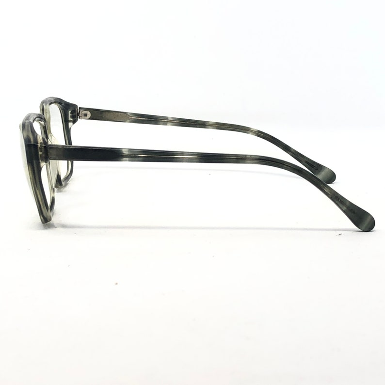 May include: A pair of eyeglasses with a gray and black marbled pattern. The frames are thick and rectangular, with a subtle cat-eye shape. The temples are thin and curve down to the ear. The lenses are clear.