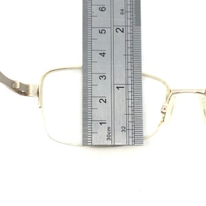 Pu&ograve; includere: Occhiali rettangolari color argento con un righello che mostra una misura di circa 2,5 cm. Gli occhiali hanno una montatura sottile e sono su uno sfondo bianco. Il righello &egrave; contrassegnato in pollici e centimetri.