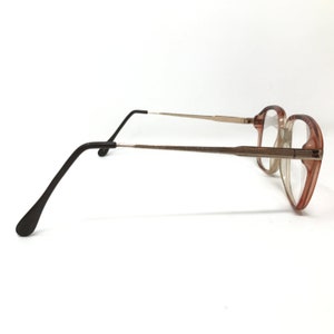 K&ouml;nnte beinhalten: Eine Brille in Braun und Gold mit schwarzem Gestell. Die Brille hat eine rechteckige Form und ist aus Kunststoff.
