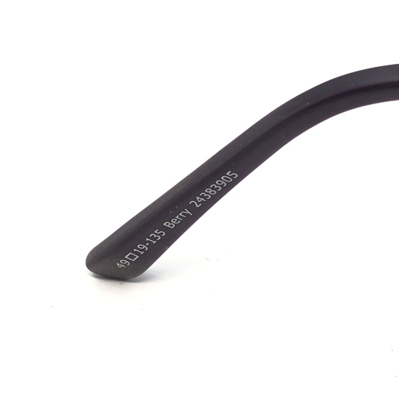 Peut inclure: Gros plan sur une branche de lunettes noire avec le texte "49▢19-135 Berry 24383905" imprim&eacute; en blanc. La branche est l&eacute;g&egrave;rement incurv&eacute;e et a une pointe arrondie. Le fond est blanc.
