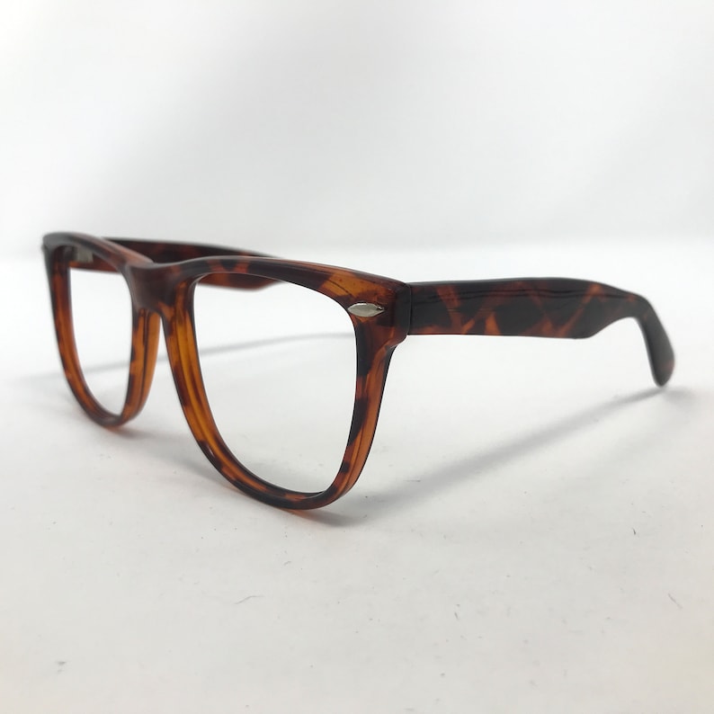 May include: A pair of eyeglasses with a classic tortoiseshell pattern. The frames are a mix of brown and amber hues, with a rectangular shape and clear lenses. The temples have a slight curve for a comfortable fit.