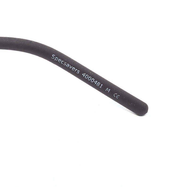 May include: Close-up of a black eyeglass arm with the text "Specsavers 4000481 M CE" printed in white. The arm is made of a matte material and has a rounded tip. The background is white.