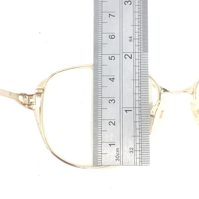 K&ouml;nnte beinhalten: Brille mit silbernem Rahmen und einem Lineal neben der Linse. Die Rahmenbreite misst etwa 5 cm. Die Brille hat ein klassisches, minimalistisches Design.