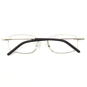 May include: A pair of rimless eyeglasses with a gold-colored metal frame and dark brown temples. The lenses are rectangular and the nose pads are clear. The glasses are set against a white background.
