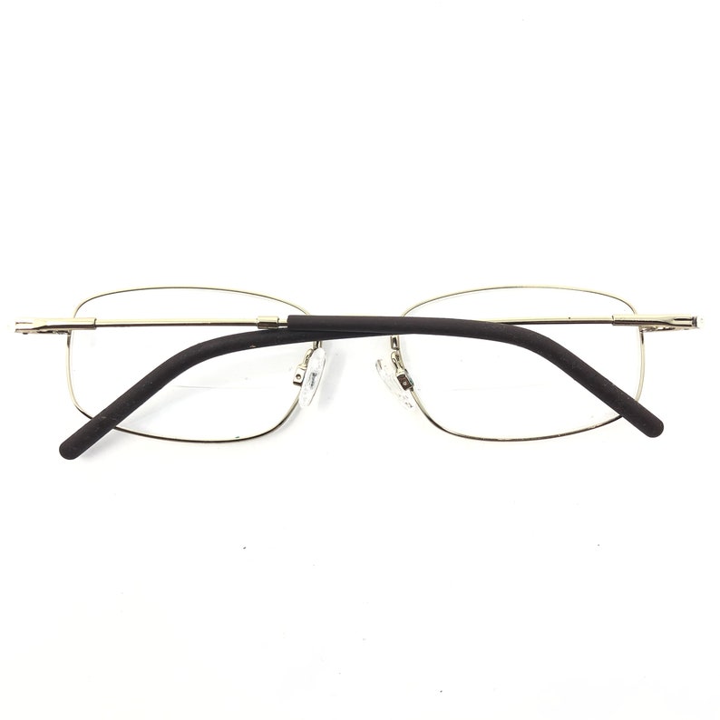 May include: A pair of rimless eyeglasses with a gold-colored metal frame and dark brown temples. The lenses are rectangular and the nose pads are clear. The glasses are set against a white background.