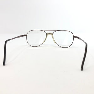 May include: Aviator-style eyeglasses with a dark brown metal frame and clear lenses. The glasses have a double bridge and thin temples that curve at the ends. The lenses are oval-shaped and the frame is a dark brown color.