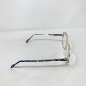 Puede incluir: Gafas con montura transparente y patillas estampadas. Las patillas presentan un dise&ntilde;o colorido con detalles en azul, morado y verde. Las gafas tienen forma de lente redonda y est&aacute;n sobre un fondo blanco.