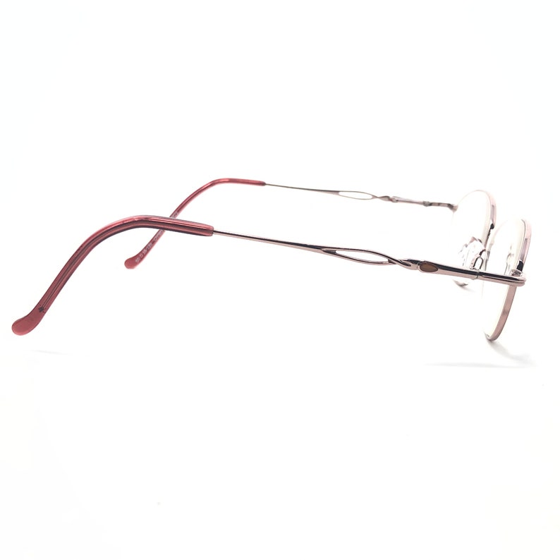 Puede incluir: Un par de gafas sin montura con un dise&ntilde;o delicado. Las monturas son plateadas y burdeos, con una forma sutil y curvada. Las patillas tienen un detalle decorativo en forma de onda. Las lentes son transparentes.