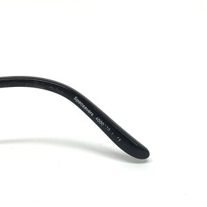 May include: Close-up of the arm of a pair of black eyeglasses. The text "Specsavers 4000-22" is printed in white on the arm. The glasses are set against a white background.