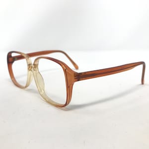 Op de afbeelding: Een vintage bril met een doorschijnend, lichtbruin montuur. De glazen zijn helder en de pootjes en het montuur hebben een iets donkerdere amberkleur. De bril heeft een klassieke, rechthoekige vorm.