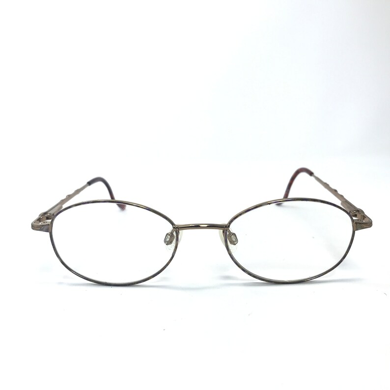 May include: A pair of oval-shaped, gold-toned spectacles with thin metal frames.