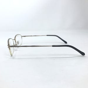May include: A pair of gold-tone metal eyeglasses with black plastic temple tips. The glasses have a rimless design and are in a side view.