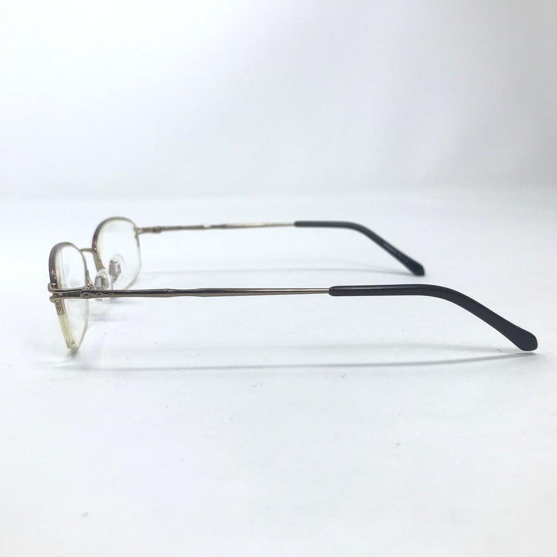 May include: A pair of gold-tone metal eyeglasses with black plastic temple tips. The glasses have a rimless design and are in a side view.
