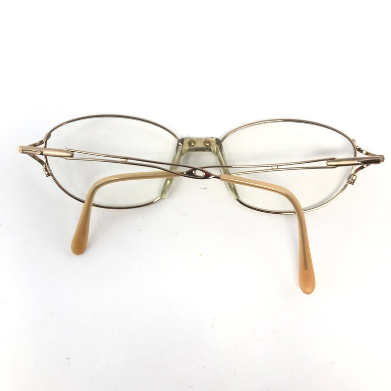 Peut inclure: Lunettes en m&eacute;tal dor&eacute; avec des verres de forme ovale et une monture fine en fil m&eacute;tallique. Les branches sont en plastique beige.